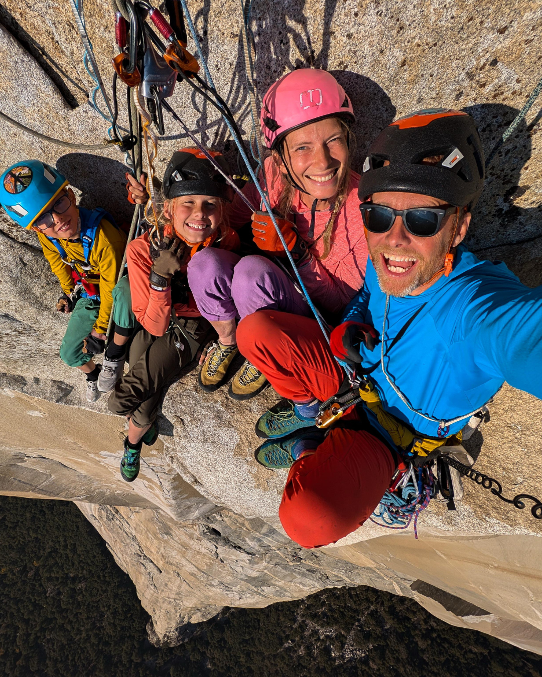 action photo of a family of people climbing up a steep cliff face, roped to the cliff